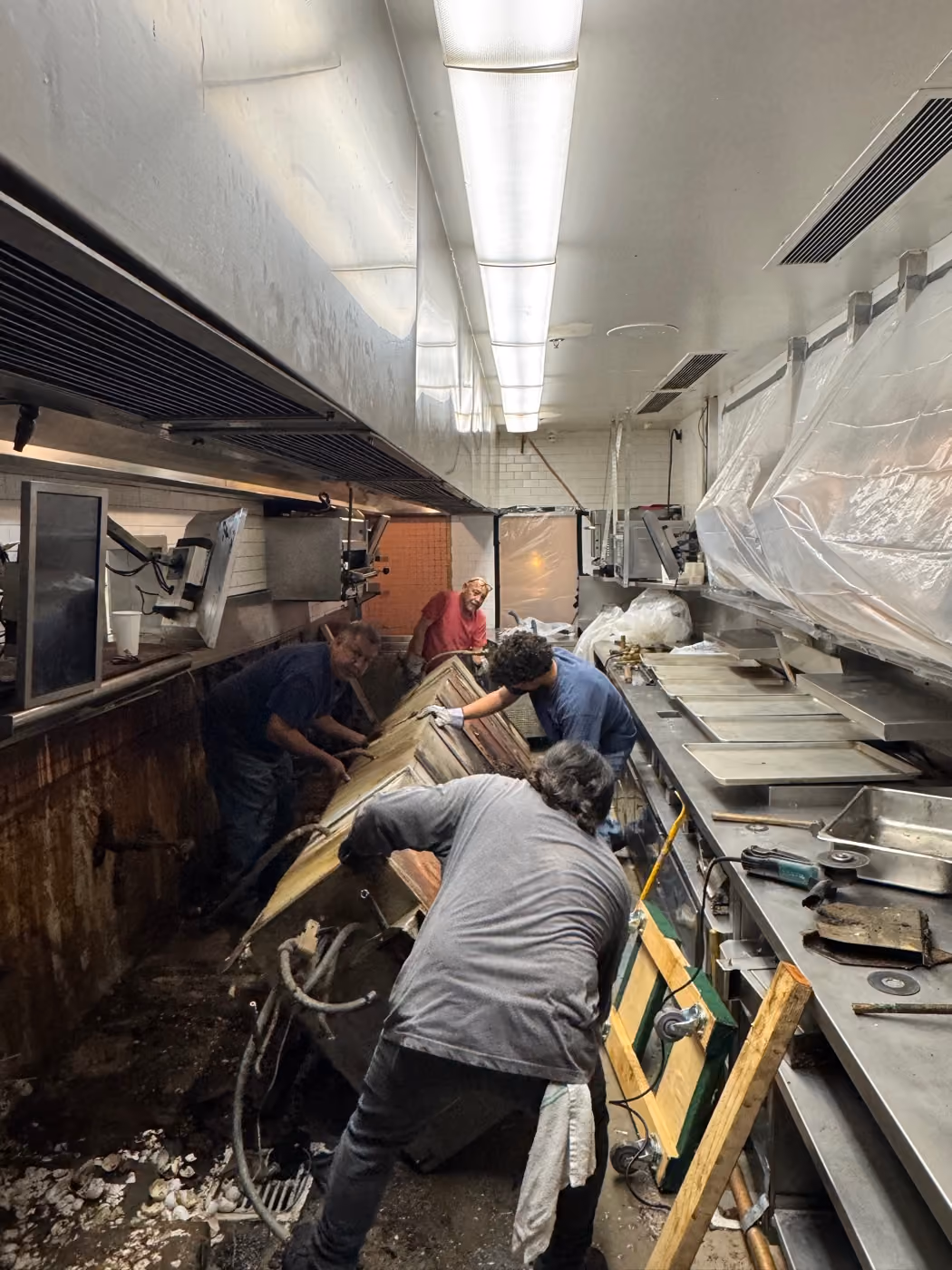 Four engineers working along a kitchen line during a strip-out, sheeting overhead