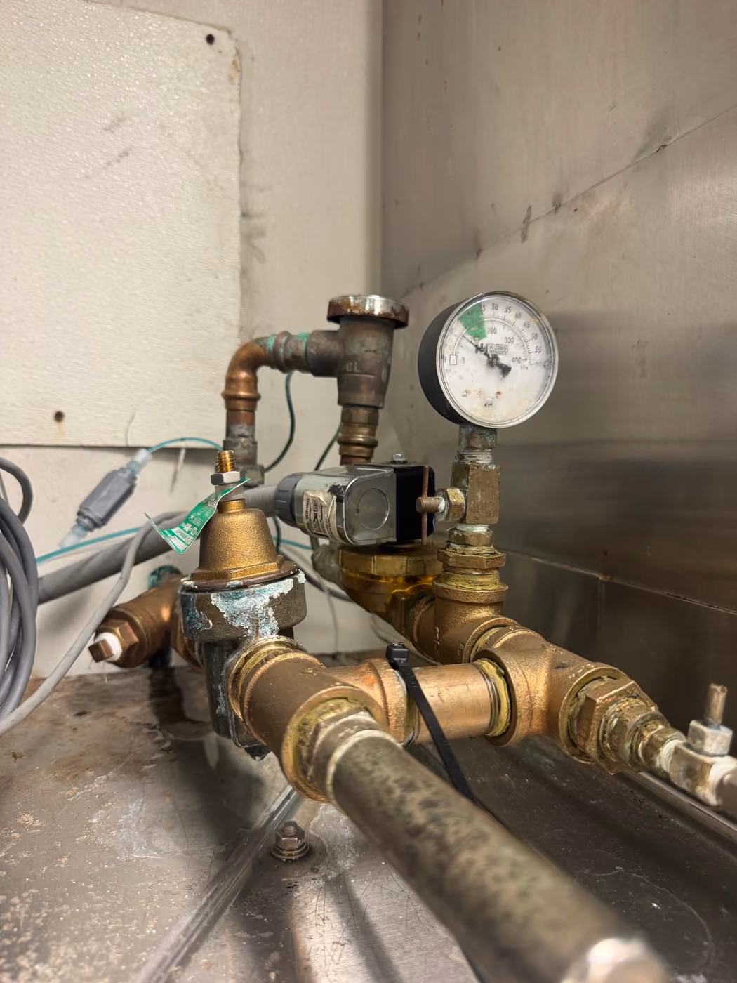 Brass gas regulator, solenoid and pressure gauge piped on a stainless surface